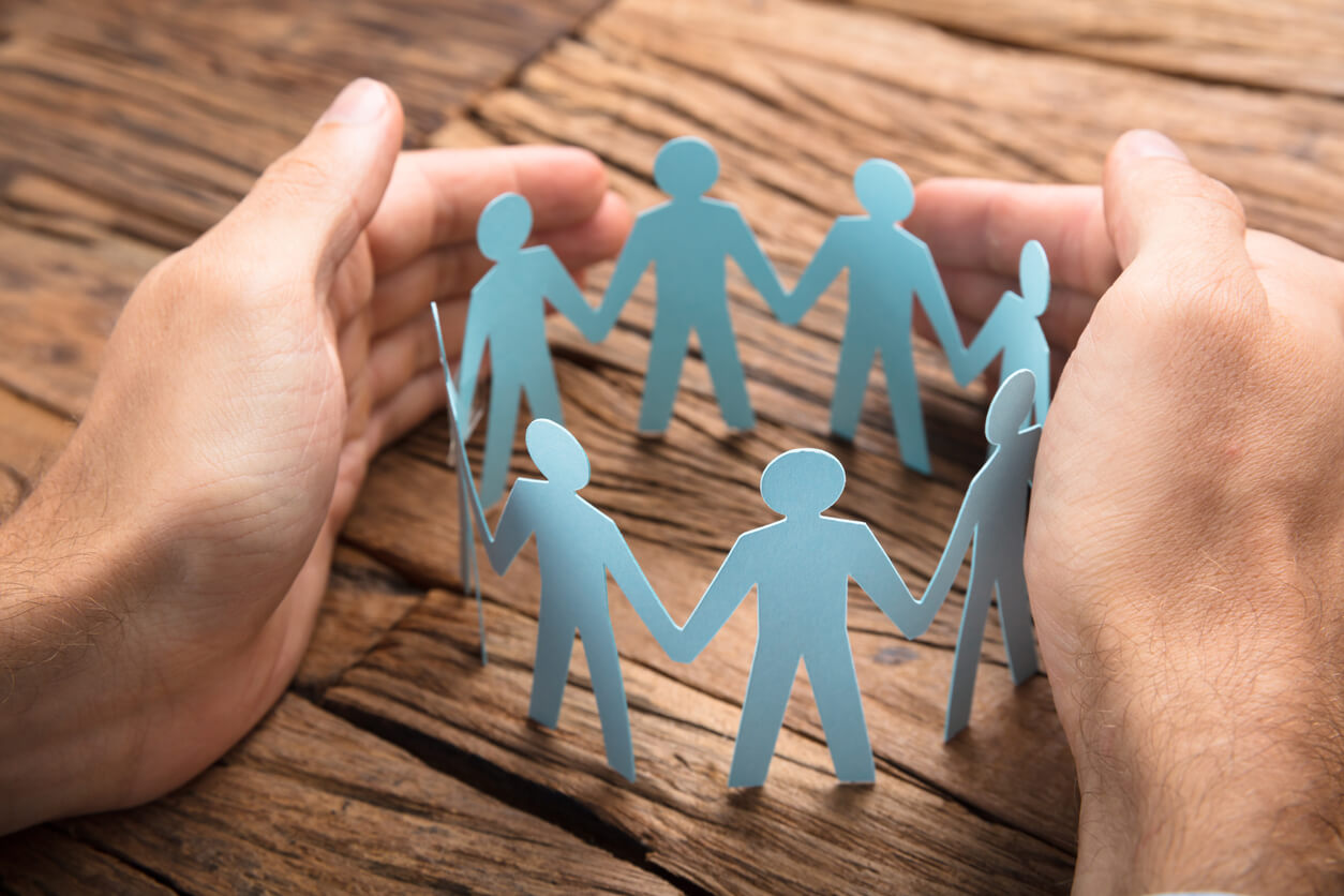 Cropped image of hands sheltering a ring of paper people on wooden table